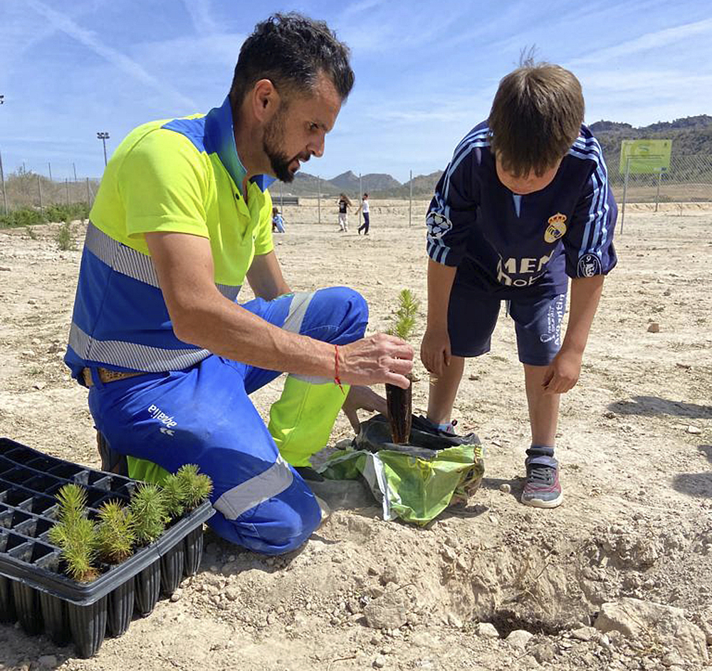 Un operario y un alumno de un colegio de Agramón (Albacete) plantan árboles en la depuradora de Hellín. 